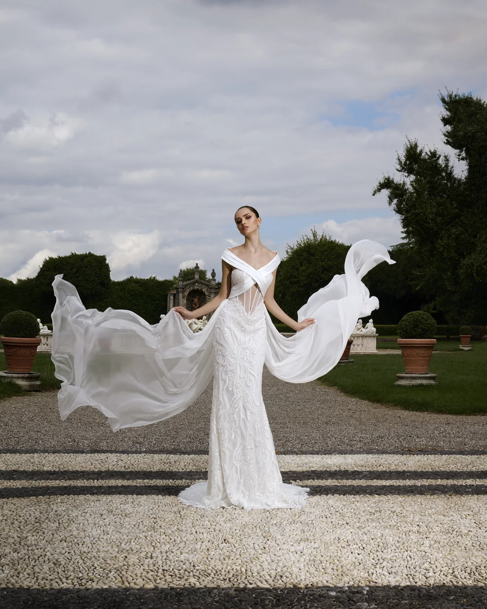 Sposa nel giardino di una villa, abito ricamato con lunghi pannelli di organza che volano nel vento