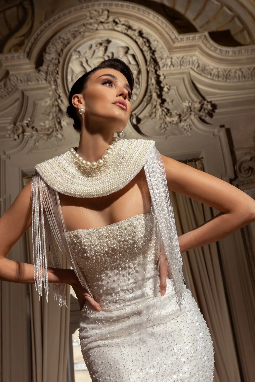 Sposa con collare di perle e frange di cristalli, sotto gli stucchi del palazzo